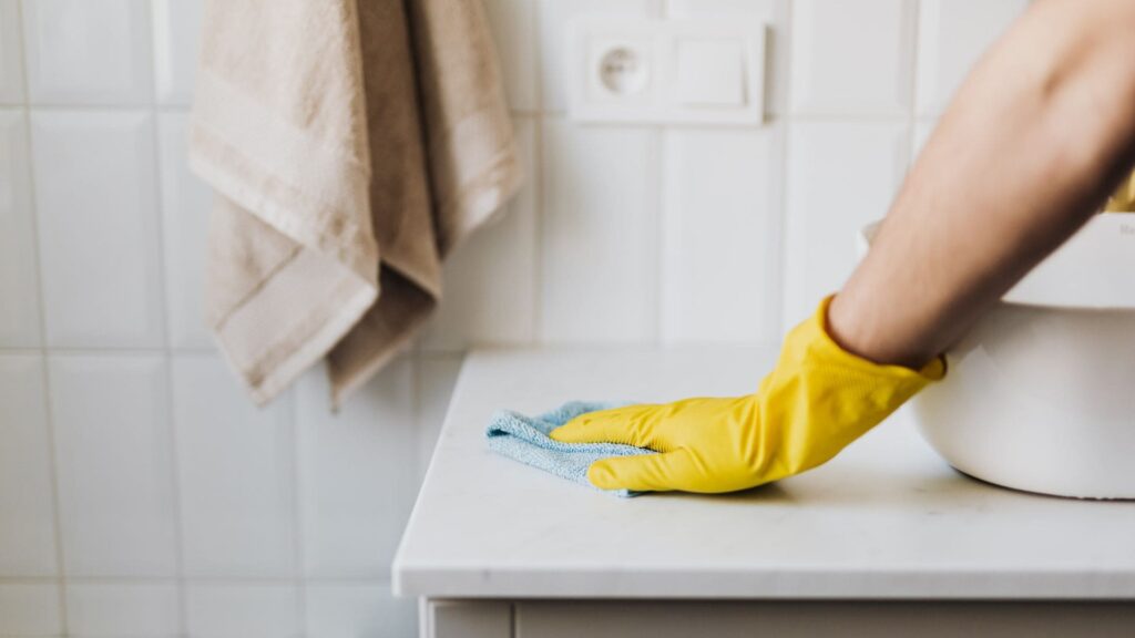 Persona usando guantes amarillos para limpiar a fondo el lavabo de un baño en un apartamento vacacional en la Costa del Sol.