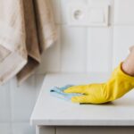 Persona usando guantes amarillos para limpiar a fondo el lavabo de un baño en un apartamento vacacional en la Costa del Sol.