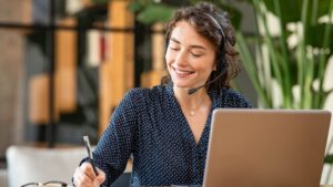 Empleada trabajando con un ordenador tomando notas y atendiendo a los clientes